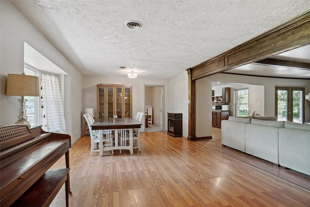 dining area with a textured ceiling, visible vents, baseboards, and light wood-type flooring