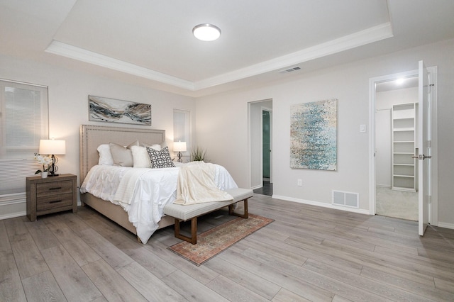 bedroom with a tray ceiling, visible vents, light wood-style flooring, and a spacious closet