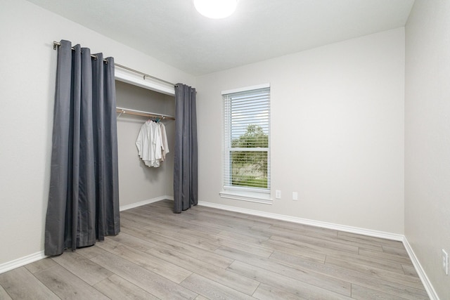 unfurnished bedroom featuring light wood-style floors, baseboards, and a closet