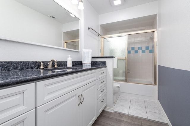 full bath featuring visible vents, vanity, marble finish floor, shower / bath combination with glass door, and toilet