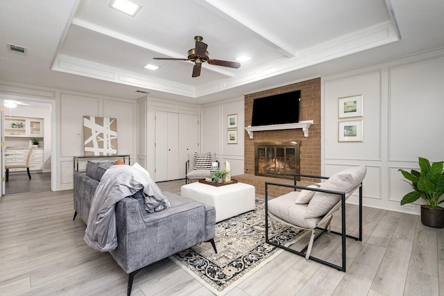 living area with ceiling fan, visible vents, light wood-type flooring, and a decorative wall