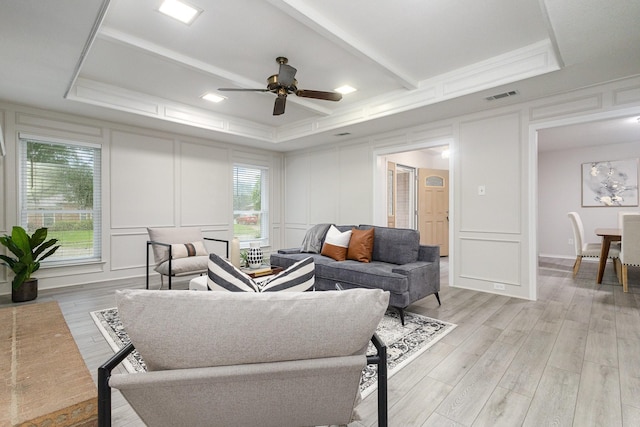 living room with a ceiling fan, visible vents, light wood-type flooring, and a decorative wall