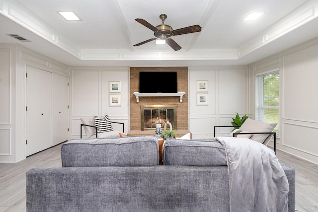 living room with ceiling fan, a decorative wall, wood finished floors, a tray ceiling, and visible vents