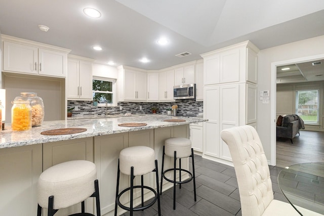 kitchen with a kitchen breakfast bar, stainless steel microwave, visible vents, and tasteful backsplash