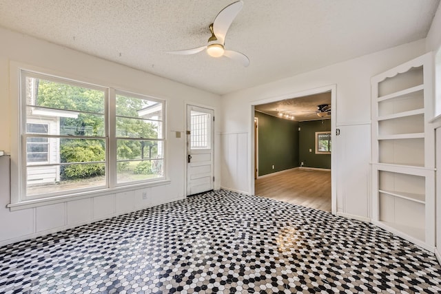 spare room with built in features, ceiling fan, a textured ceiling, and a wealth of natural light