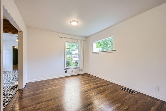 empty room with dark wood-style flooring, baseboards, and visible vents