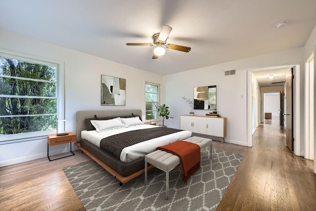 bedroom featuring baseboards, wood finished floors, visible vents, and multiple windows