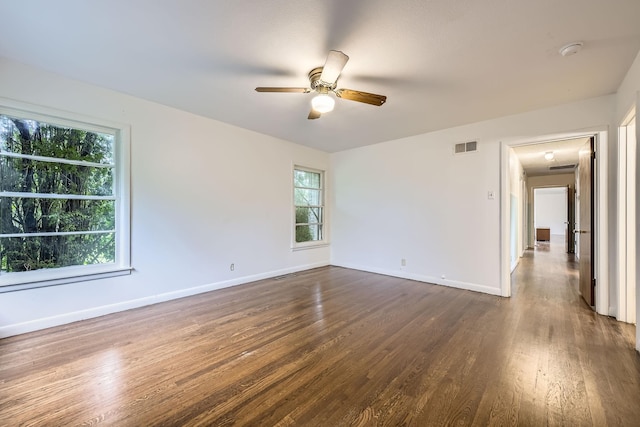 empty room featuring baseboards, a ceiling fan, dark wood-type flooring, and a wealth of natural light