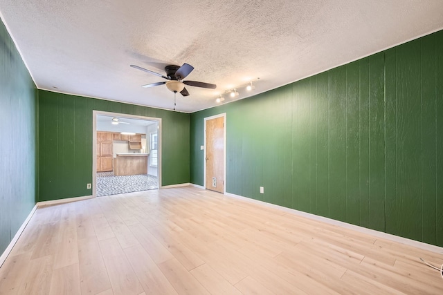 empty room featuring track lighting, a ceiling fan, a textured ceiling, and wood finished floors