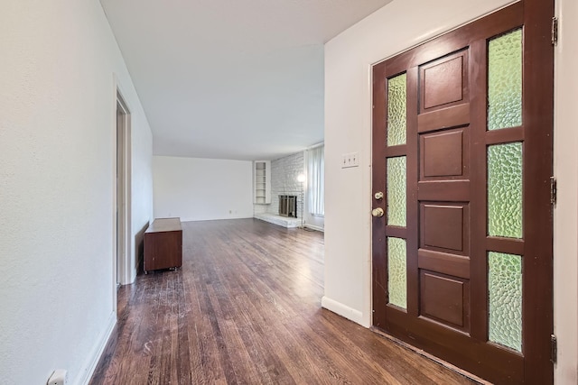 foyer entrance with baseboards, a brick fireplace, and dark wood-style floors