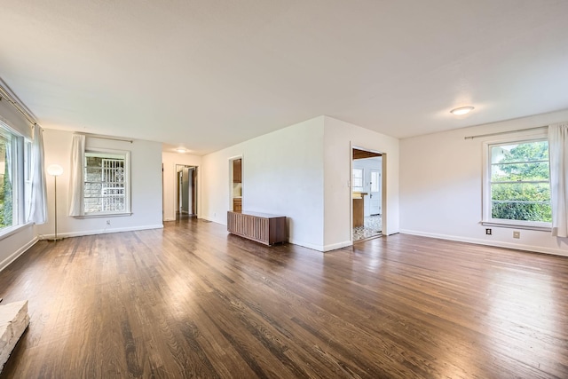 unfurnished living room with dark wood-type flooring, baseboards, and a healthy amount of sunlight