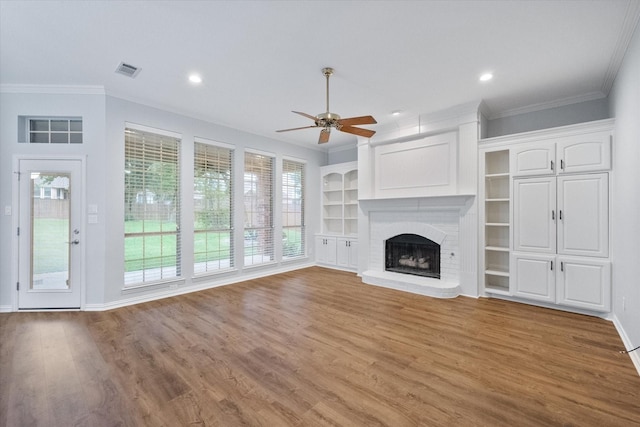 unfurnished living room featuring ceiling fan, visible vents, a brick fireplace, wood finished floors, and ornamental molding