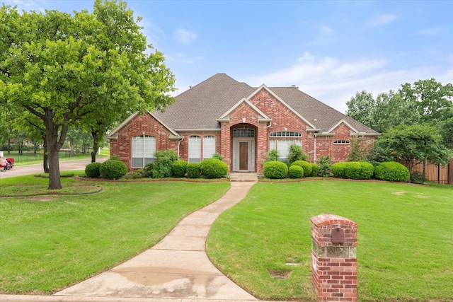 view of front of home featuring brick siding, a shingled roof, and a front lawn