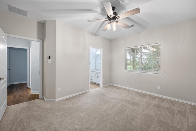 unfurnished bedroom with baseboards, light colored carpet, ensuite bath, and visible vents