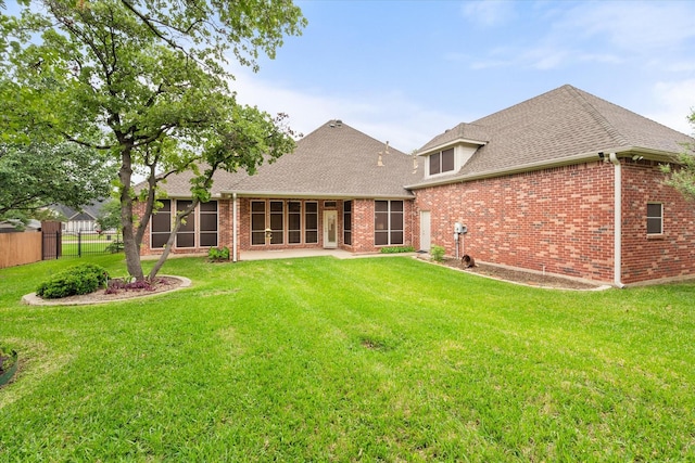 back of house featuring a lawn, brick siding, fence, and a sunroom
