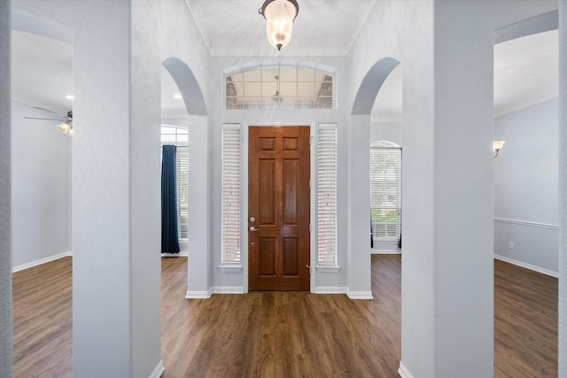 entryway with arched walkways, baseboards, ornamental molding, and wood finished floors