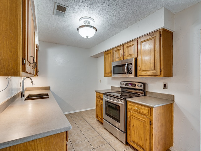 5005 Drew Ct, Arlington, TX 76017 - kitchen with a sink, a textured ceiling, brown cabinetry, stainless steel appliances, and visible vents