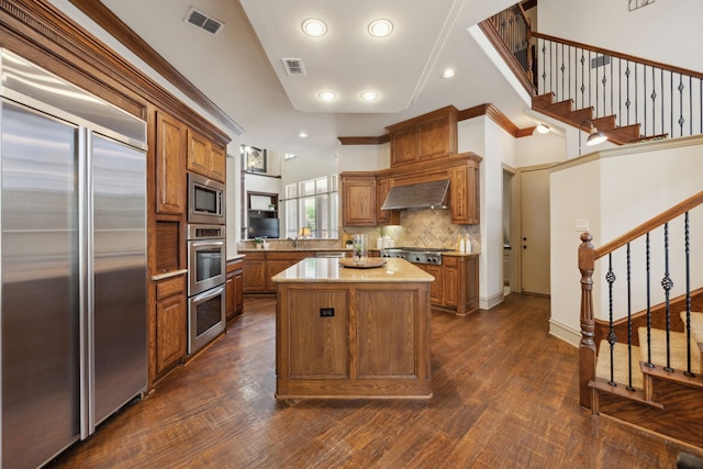 1041 Bandelier Dr, Allen, TX 75013 - kitchen with built in appliances, wall chimney exhaust hood, brown cabinetry, decorative backsplash, and recessed lighting