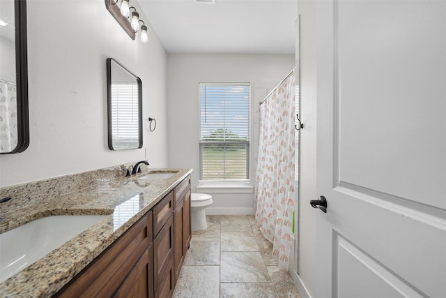 bathroom featuring double vanity, toilet, baseboards, and a sink