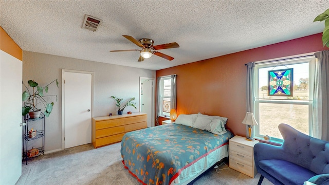 bedroom with ceiling fan, light carpet, a textured ceiling, and visible vents