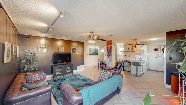 living room featuring a textured ceiling, a ceiling fan, baseboards, light tile patterned floors, and visible vents