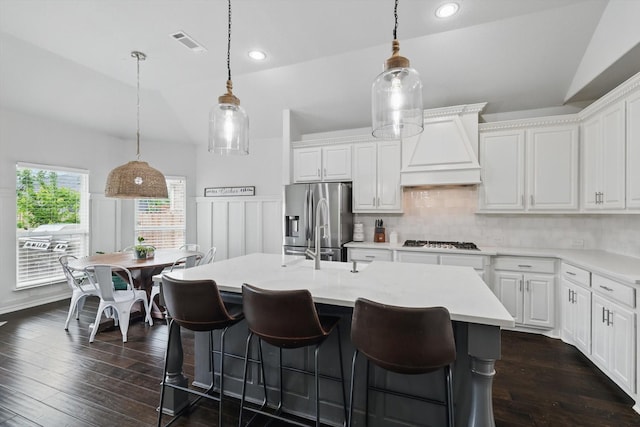 kitchen featuring visible vents, lofted ceiling, gas cooktop, stainless steel fridge with ice dispenser, and custom range hood