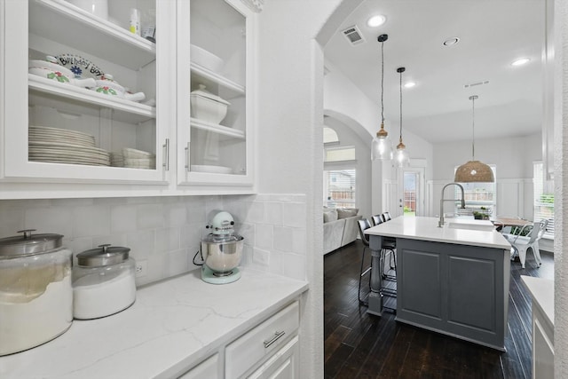 kitchen with visible vents, dark wood-type flooring, arched walkways, white cabinets, and a sink