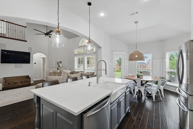 kitchen with appliances with stainless steel finishes, a sink, arched walkways, gray cabinets, and a ceiling fan