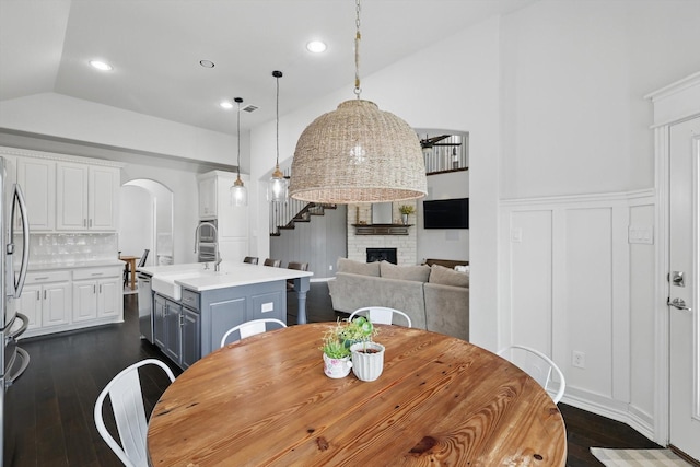 dining room featuring a fireplace, stairway, arched walkways, dark wood finished floors, and vaulted ceiling
