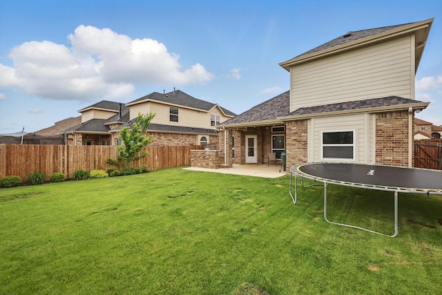 rear view of property with fence, a trampoline, brick siding, a patio area, and a yard