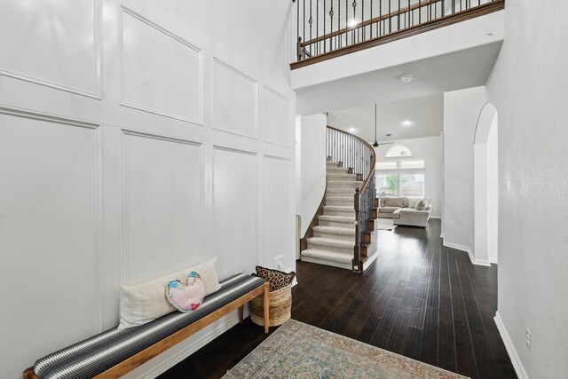 foyer featuring a towering ceiling, arched walkways, stairway, baseboards, and hardwood / wood-style floors