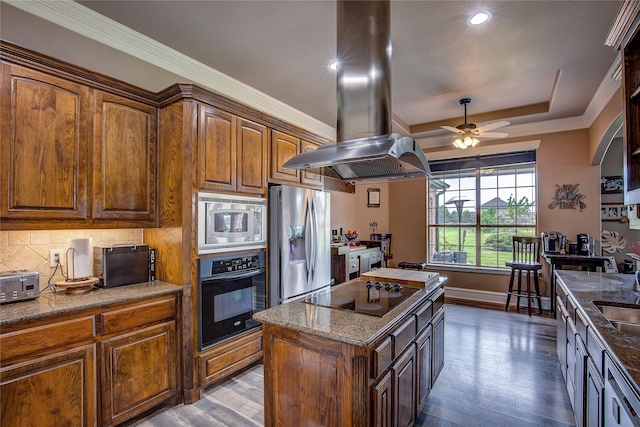 kitchen featuring a raised ceiling, a ceiling fan, island range hood, wood finished floors, and black appliances