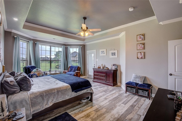 bedroom with ceiling fan, a raised ceiling, baseboards, light wood-type flooring, and ornamental molding