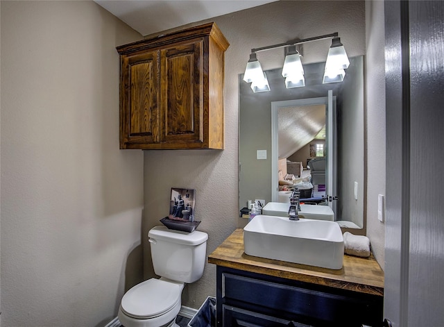 half bathroom featuring vanity, a textured wall, ensuite bathroom, and toilet