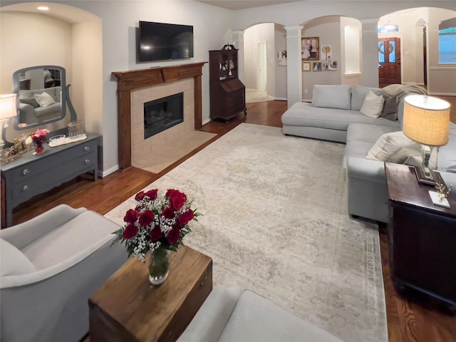 living room with wood finished floors, baseboards, ornate columns, a tile fireplace, and arched walkways