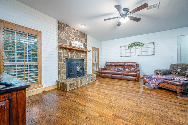 living area with visible vents, wood walls, wood finished floors, a stone fireplace, and ceiling fan
