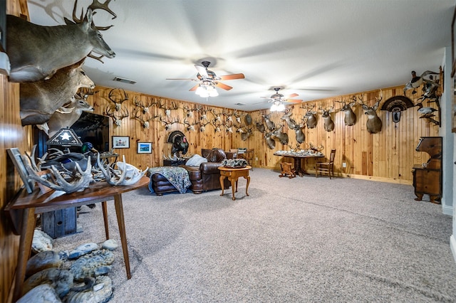 interior space featuring wooden walls, a ceiling fan, carpet flooring, and visible vents