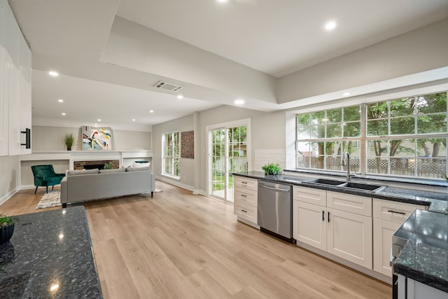 kitchen with white cabinets, a sink, light wood finished floors, dishwasher, and dark stone countertops