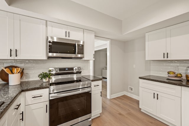 kitchen with backsplash, appliances with stainless steel finishes, baseboards, dark stone countertops, and white cabinetry