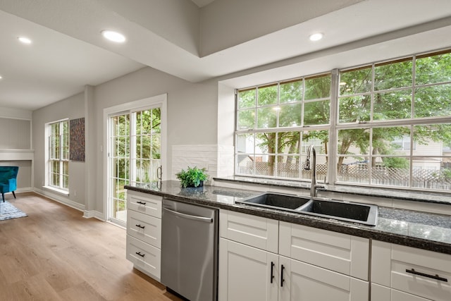 kitchen featuring white cabinets, a sink, dark stone counters, light wood-type flooring, and stainless steel dishwasher