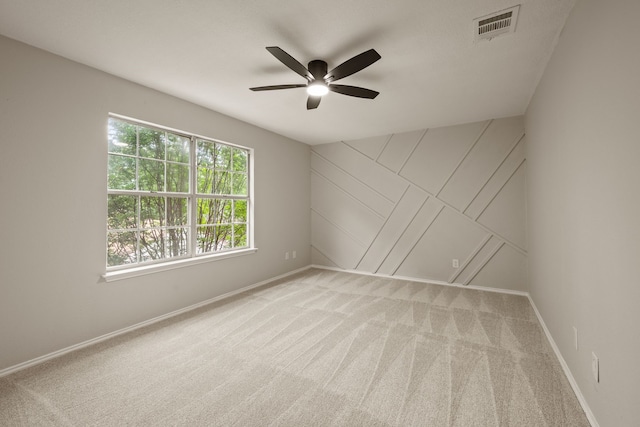 spare room with a ceiling fan, light colored carpet, visible vents, and baseboards