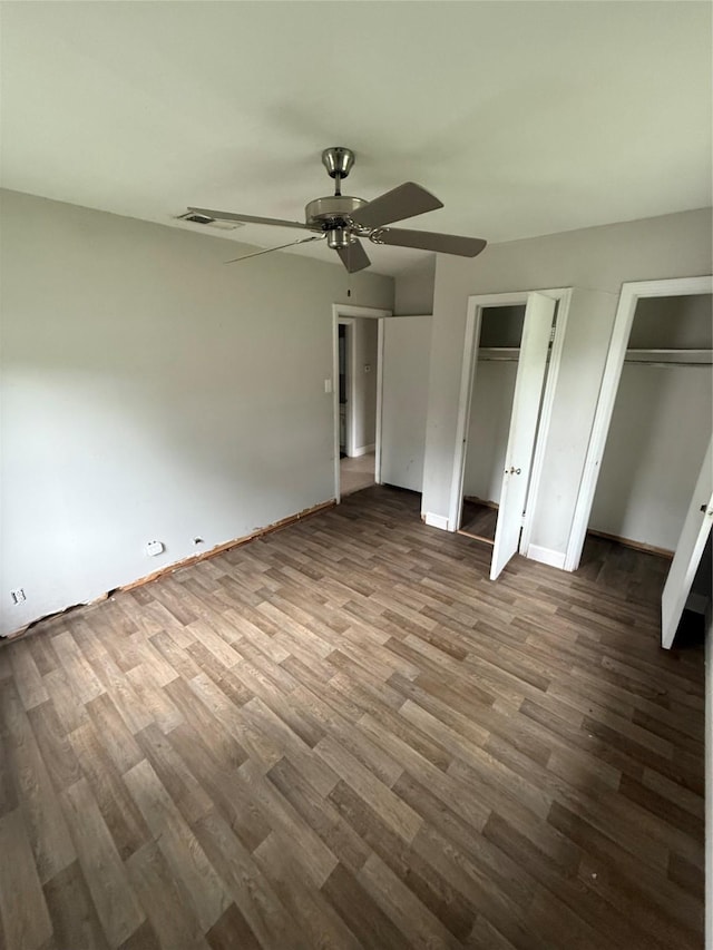 unfurnished bedroom featuring two closets, a ceiling fan, baseboards, and wood finished floors