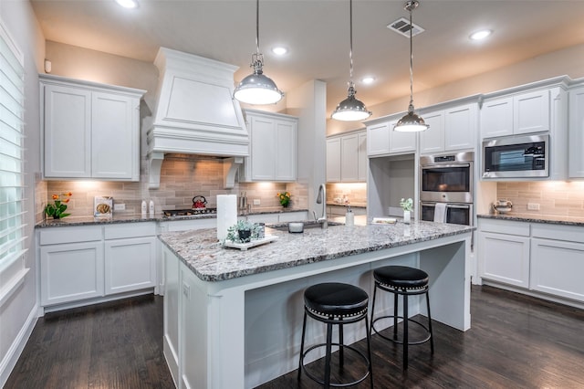kitchen featuring visible vents, appliances with stainless steel finishes, tasteful backsplash, premium range hood, and white cabinetry