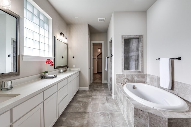 bathroom with visible vents, double vanity, a walk in closet, a bath, and a sink