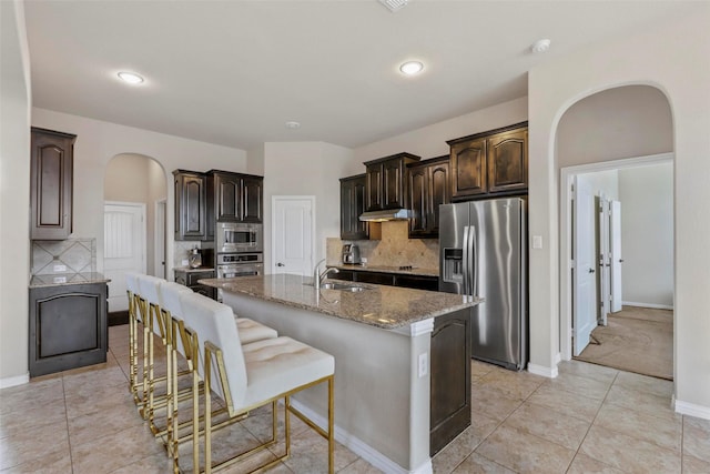 kitchen with arched walkways, stone counters, appliances with stainless steel finishes, and dark brown cabinets