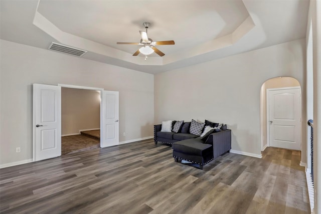 living area with visible vents, wood finished floors, baseboards, ceiling fan, and a tray ceiling