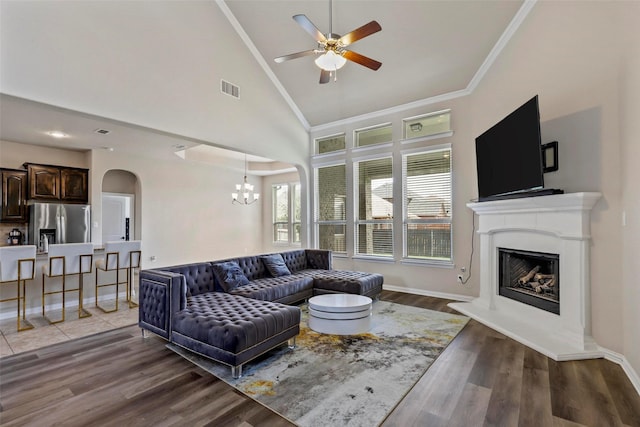 living room featuring visible vents, arched walkways, a fireplace with raised hearth, ceiling fan with notable chandelier, and light wood finished floors