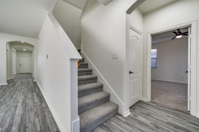 staircase featuring baseboards, arched walkways, ceiling fan, and wood finished floors