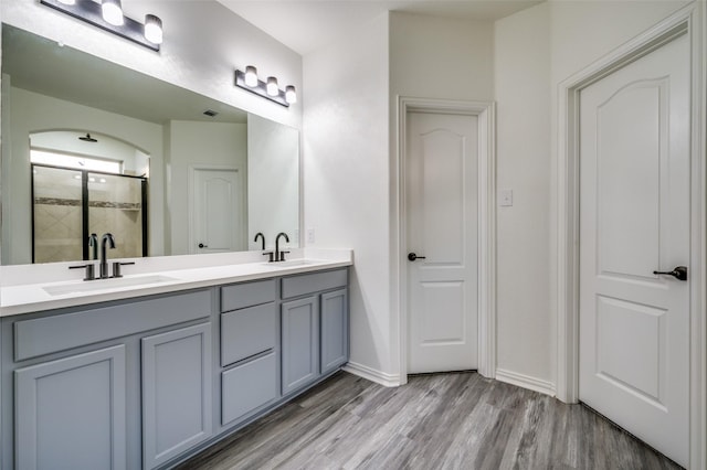 bathroom with a sink, double vanity, tiled shower, and wood finished floors
