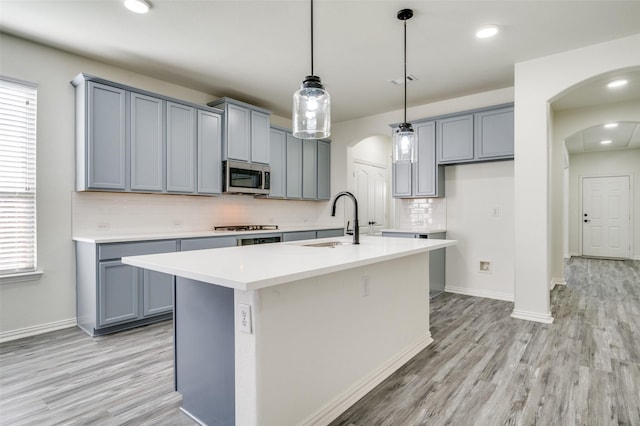 kitchen with a sink, appliances with stainless steel finishes, light wood-style floors, and arched walkways